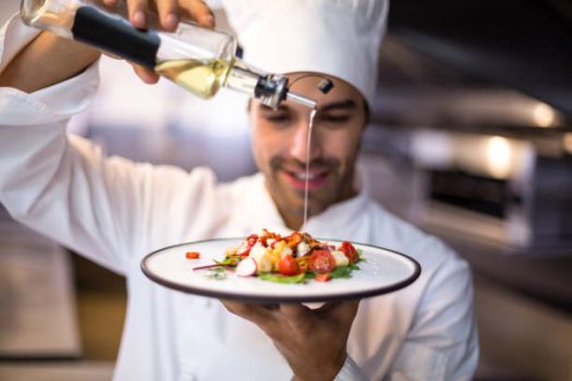 Handsome chef pouring olive oil on meal in a commercial kitchen
