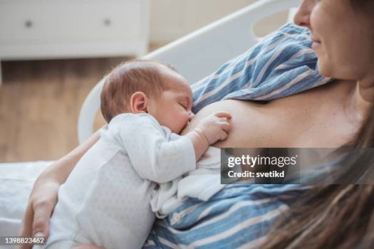 Mother breastfeeding baby boy at hospital bed.