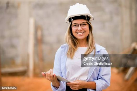 Portrait of a beautiful engineer woman with digital tablet on a construction site looking at camera and smiling
