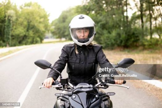 Young woman riding a motorcycle on a road. About 25 years old, Caucasian female.