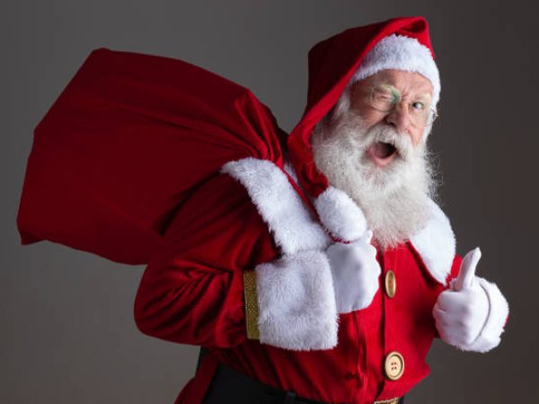 Santa Claus in eyeglasses is looking at camera and smiling, on gray background