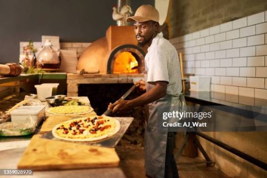 Chef making pizzas in a commercial kitchen. Cook making pizza at a restaurant and grabbing it to put it in the oven.