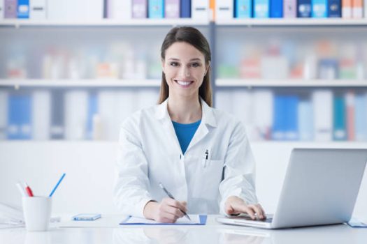 Young smiling female doctor sitting at office desk and working with a laptop Young smiling female doctor sitting at office desk and working with a laptop