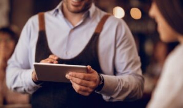 Close-up of waiter taking order on touchpad while talking to a guest in a pub.