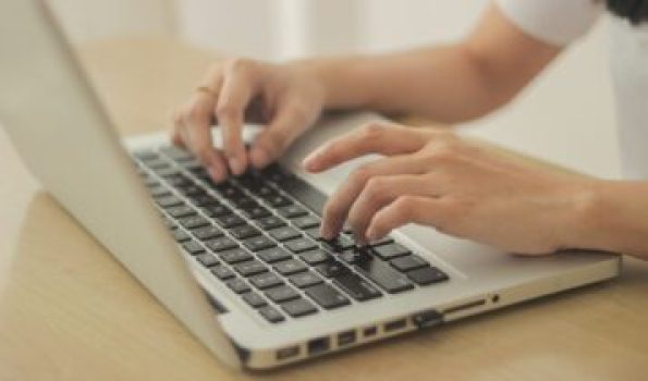 A person sitting in front of a desk and typing on the keyboard of the laptop