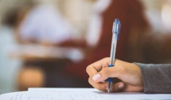 Close up hand of student reading and writing exam with stress in classroom.